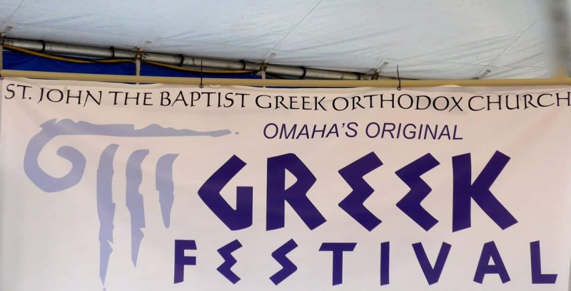 A white banner with blue text promoting Omaha’s Original Greek Festival, one of many summer festivals in Omaha.